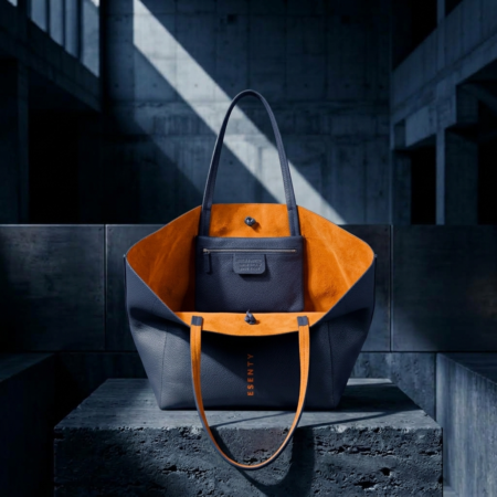 NAVY MINIMALIST TOTE BAG WITH BRIGHT ORANGE SUEDE LINING OPEN ON A BRUTALIST CONCRETE PODIUM