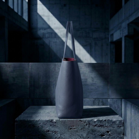 SIDE VIEW OF NAVY MINIMALIST TOTE BAG WITH DEEP BURGUNDY SUEDE LINING ON A BRUTALIST CONCRETE BLOCK