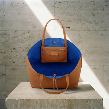 TAN MINIMALIST TOTE BAG FROM ORGANIC TAN COLLECTION WITH ROYAL BLUE LINING PLACED ON A BRUTALIST CONCRETE PODIUM